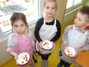 3 Kinder zeigen kleine Schälchen mit leckerem Dessert