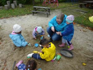 Kinder und eine Erzieherin im Sandkasten
