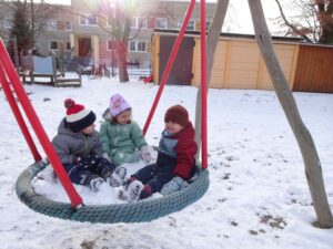 3 Kinder sitzen im Winter draußen in der Netzschaukel