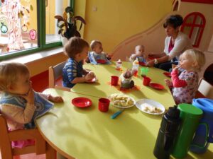 Kleinkinder am Tisch beim Essen mit einer Erzieherin
