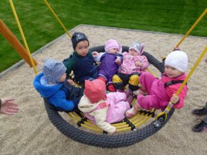 mehrere kleine Kinder sitzen in einer Nestschaukel