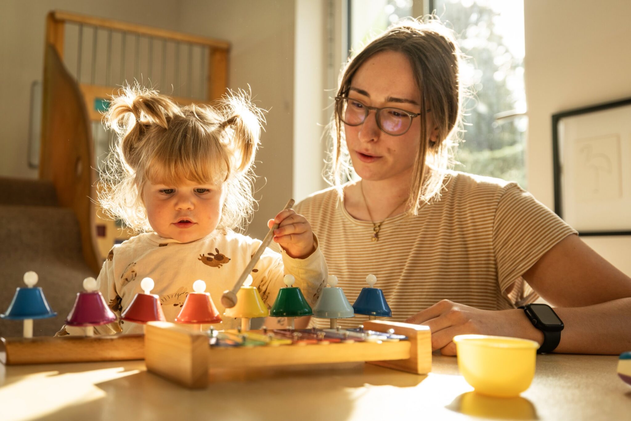 ein kleines Mädchen und eine Erzieherin am Glockenspiel