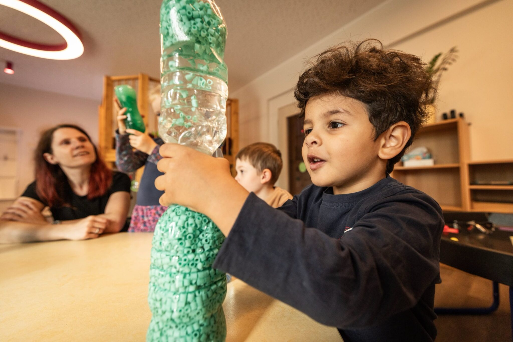 mehrere Kinder und eine Erzieherin am Tisch mit Flaschenexperiment