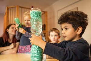 mehrere Kinder und eine Erzieherin am Tisch mit Flaschenexperiment