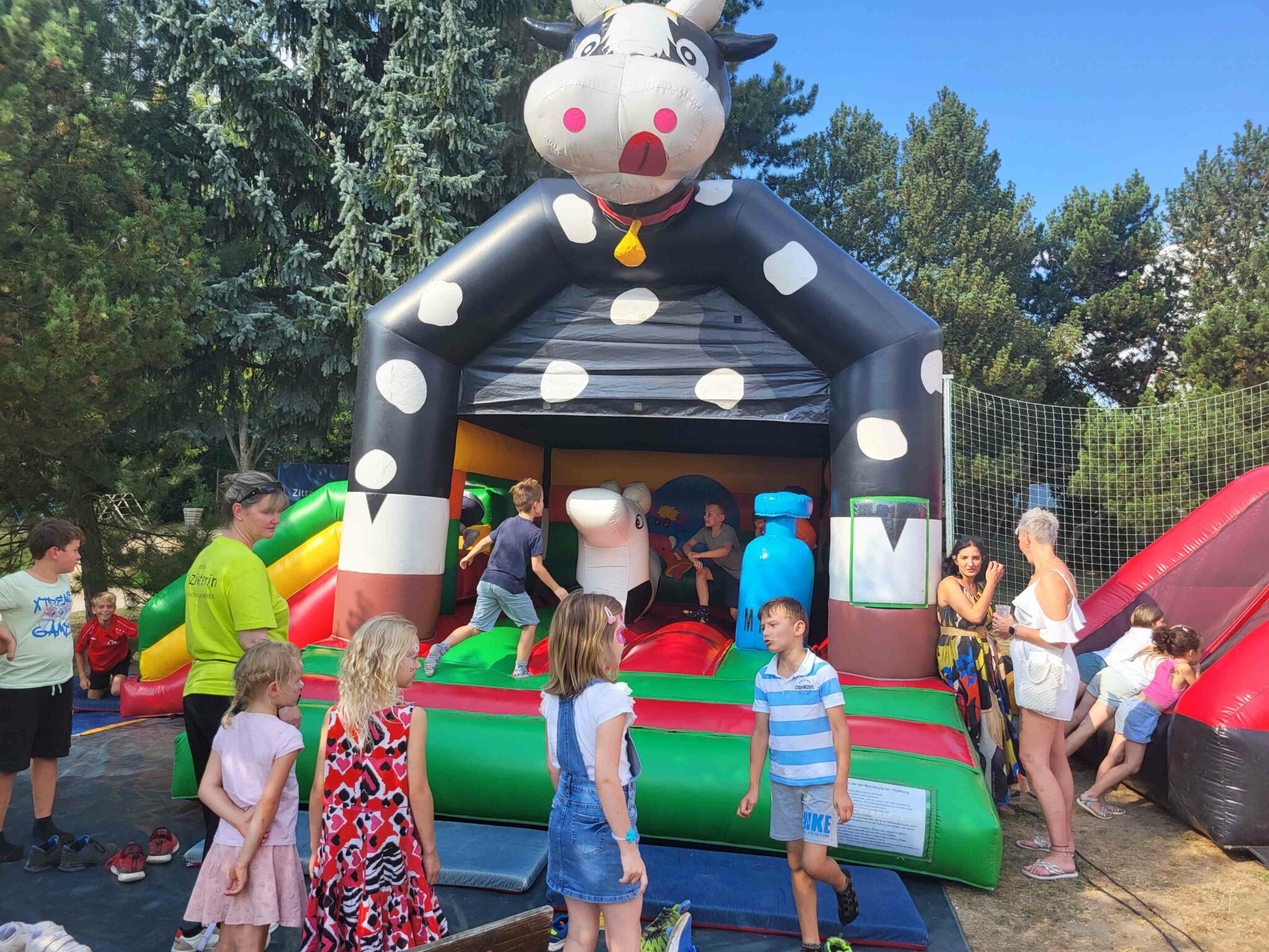 Viele Kinder vor uns auf einer Hüpfburg in Form einer riesigen Kuh.