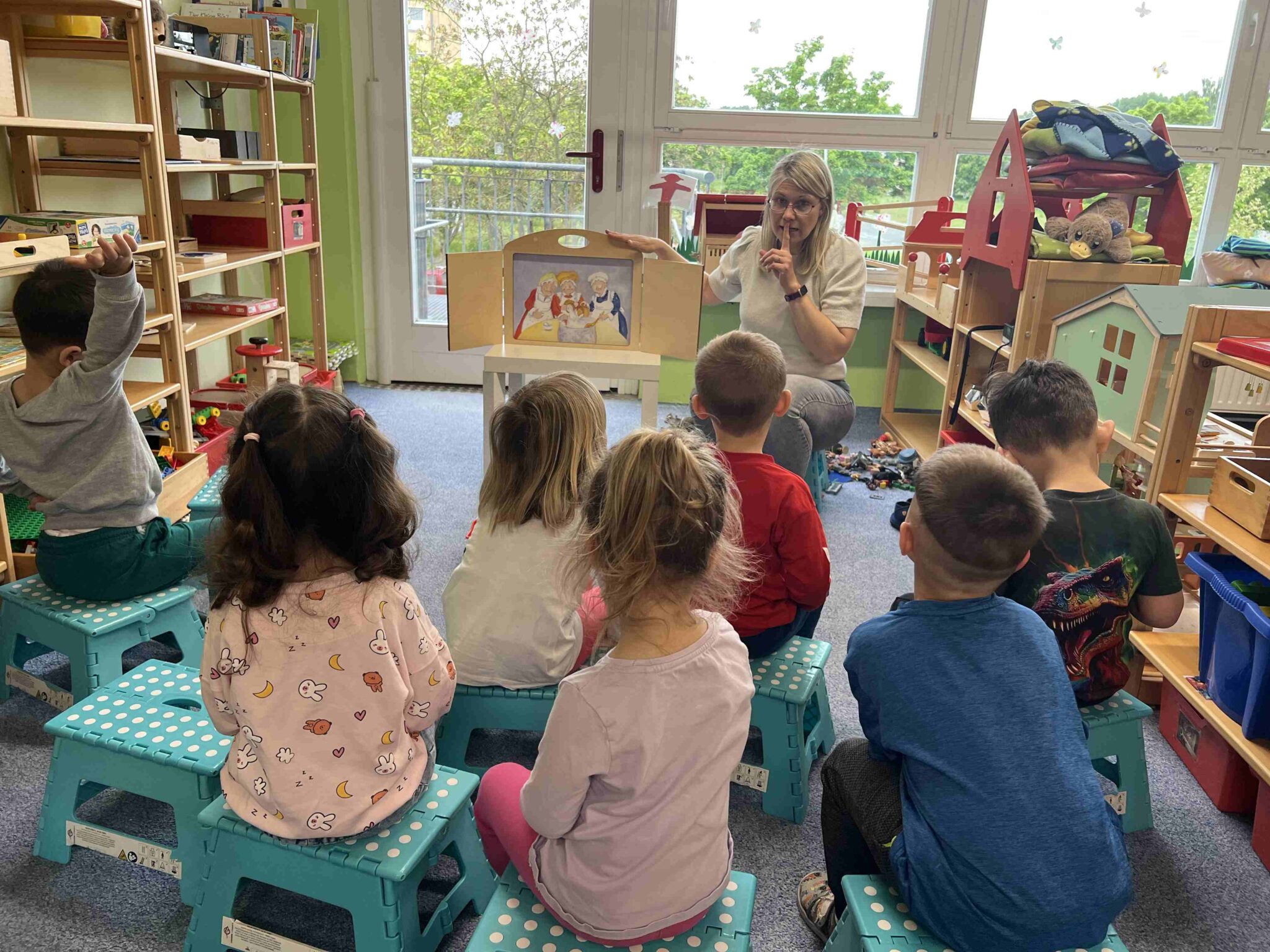 Erzieherin sitzt vor Kindern an einem Puppentheater und erzählt eine Geschichte während Kinder gespannt zuhören.