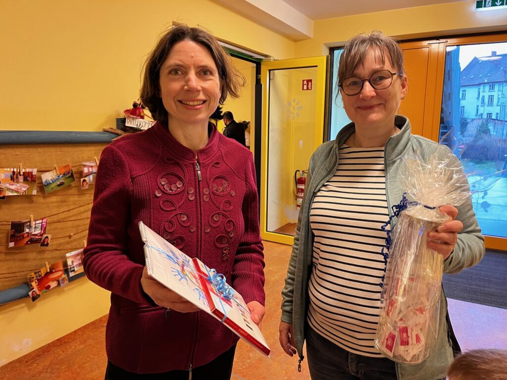 Zwei Frauen blicken in die Kamera und halten Geschenke in ihren Händen.