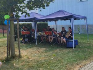 Ein Akkordeon-Orchester sitzt während ihres Spieles unter einem Pavillon im Schatten.