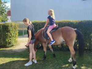 Ein Kind auf einem Pony, welches von einem größeren Mädchen geführt wird.