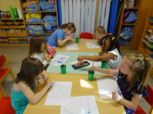 Kinder sitzen links und rechts an einem Tisch, malen und basteln gemeinsam.