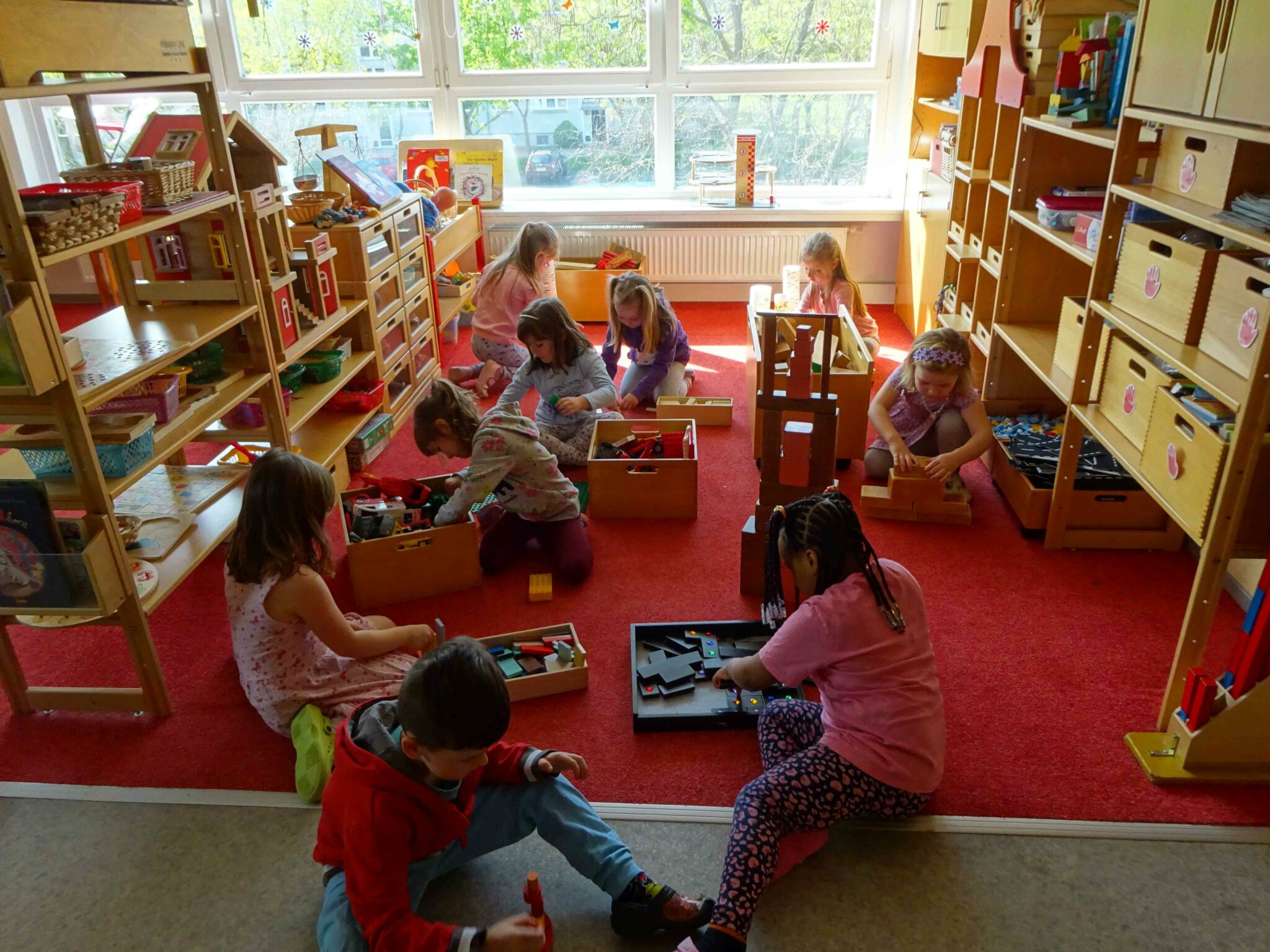 Kinder sitzen auf einem roten Teppich und spielen gemeinsam mit Bausteinen.