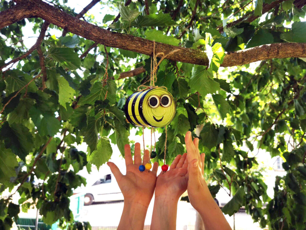 Insektenhotel in Form einer Biene hängend im Baum mit 3 Händen darunter